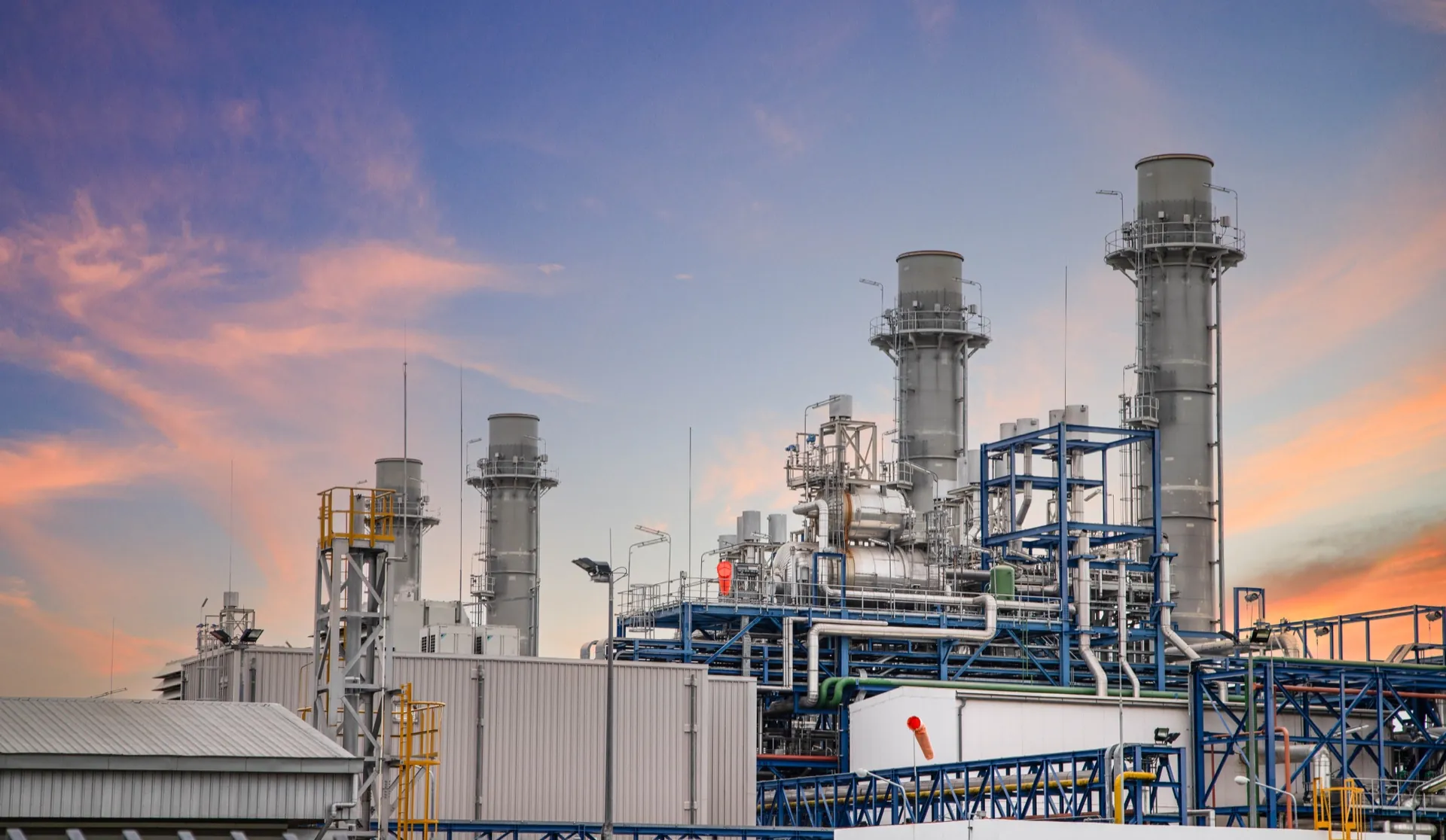 Industrial facility with tall stacks, steel structures, and interconnected pipes beneath an evening sky.